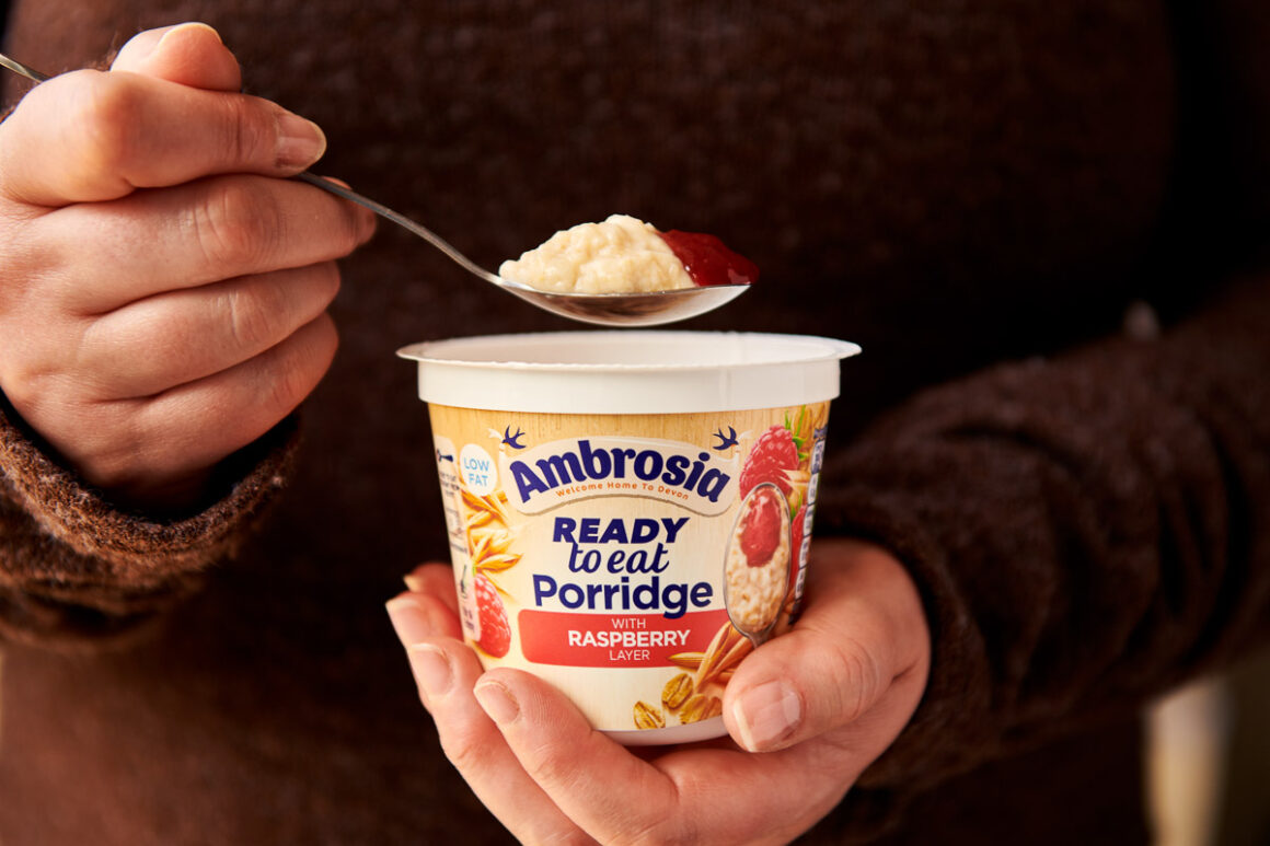 a ladies hand holding a spoonful of ambrosia raspberry ready to eat porridge