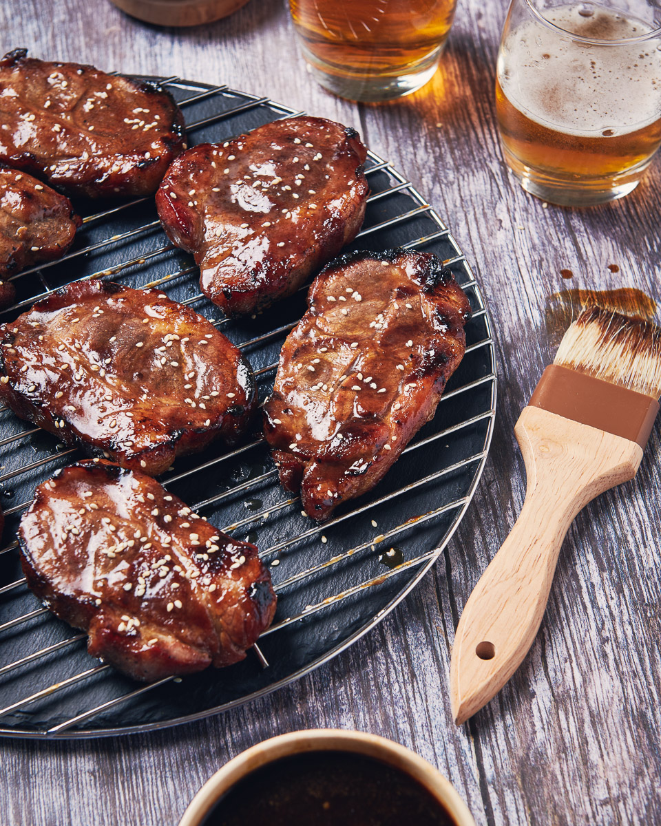a group of pork chops coated with asian themed sauce and sesame seed sprinkled on. shot by professional food photographer for coeliac uk in connection with delicious by design