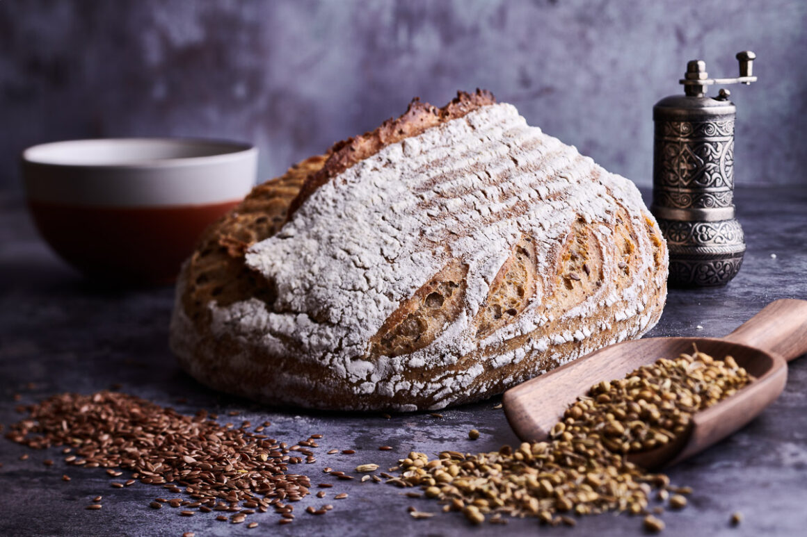 moody artistic photograph of a loaf of sourdough with scattered seeds. shot by professional food photographer for elaine boddy and page street publishing