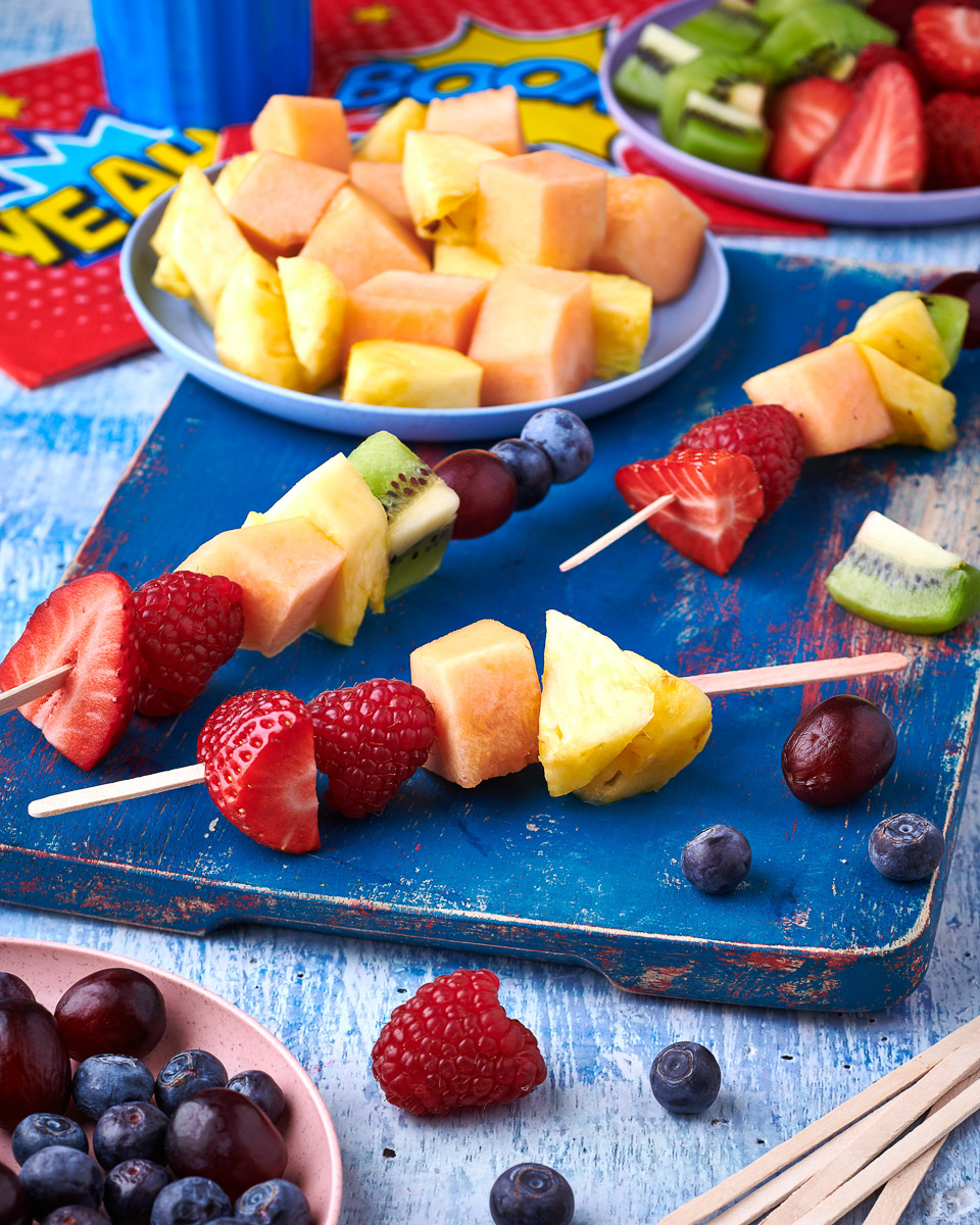 bright and colourful shot of a variety of fruit on skewers in a fun setting. shot by professional food photographer for coeliac uk in connection with delicious by design