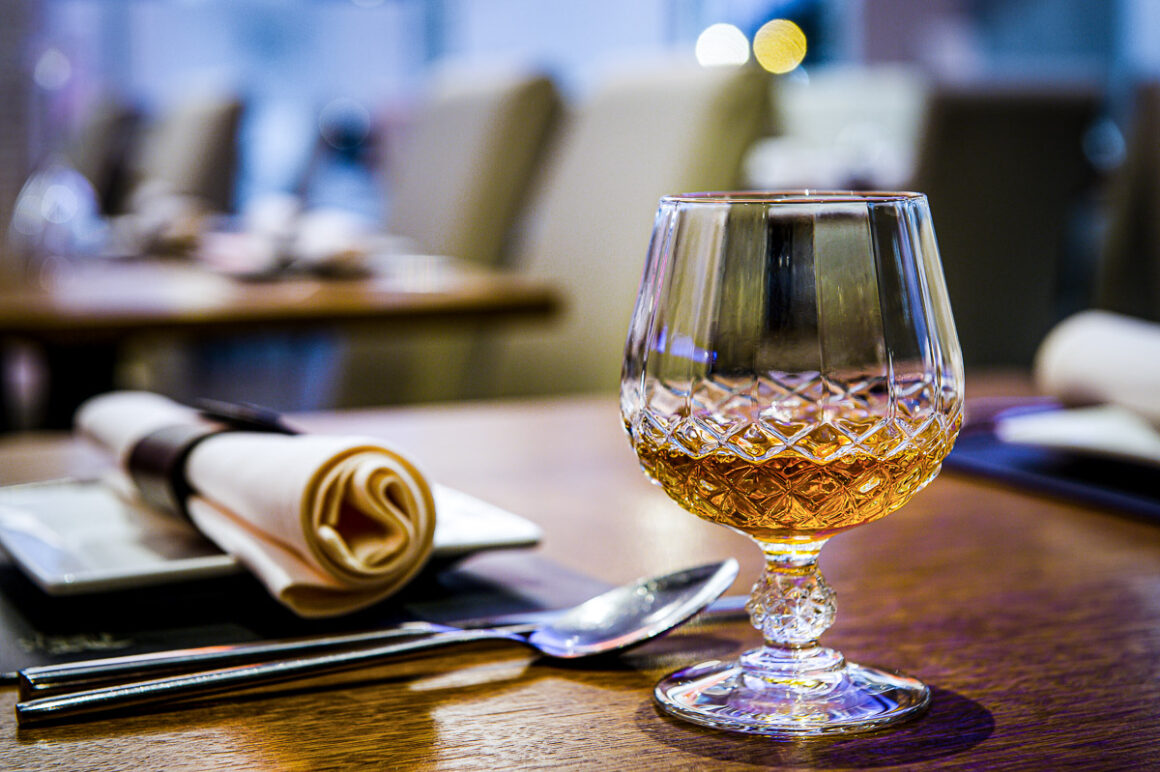 a moody restaurant shot of a glass of brand on a table with background out of focus. shot by professional food photographer