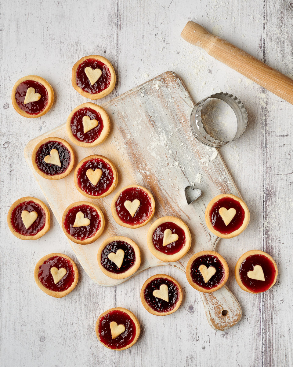 variety of jam tarts with love heart pastry centres, shot top down on a light background with rolling pin and cutter