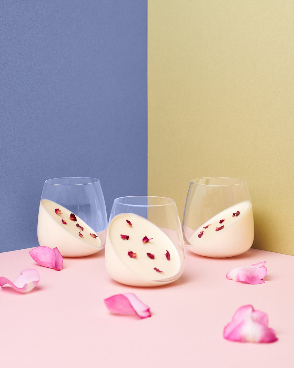 arty shot of panna cotta in three separate tumblers with rose petals strewn around. shot by professional food photographer for coeliac uk in connection with delicious by design