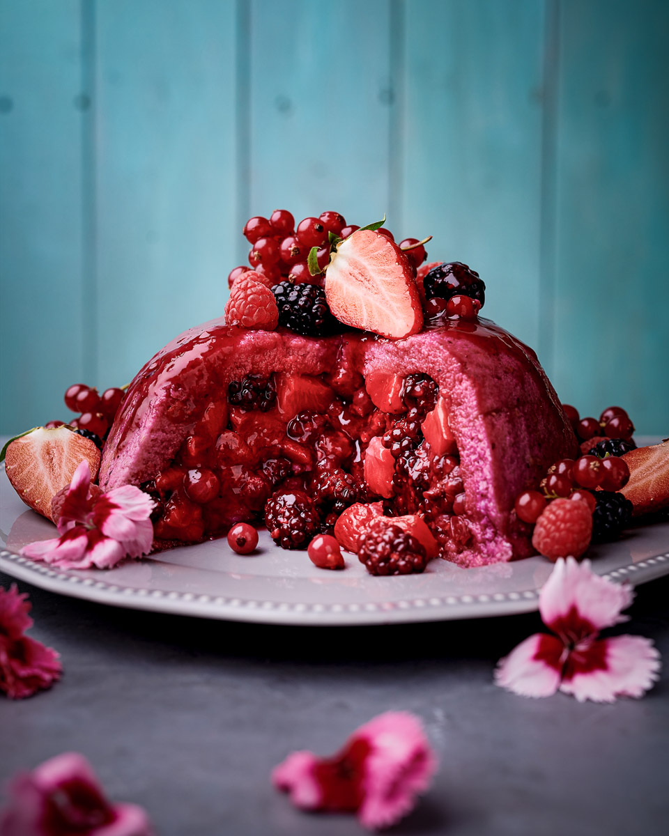summer pudding with a large chunk removed, showing fruit inside and decorated with fruit and flowers, shot by professional food photographer for coeliac uk