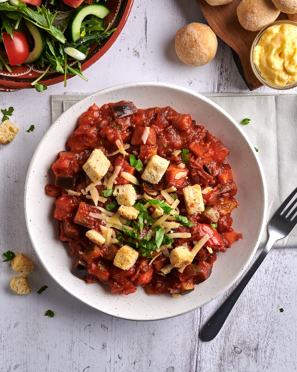 top down image of a bowl of ratatouille with bread croutons, a side salad and some scattered garnish. shot by professional food photographer for premier foods in connection with delicious by design